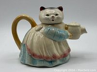Front view of ceramic cat teapot holding small teapot, white and pastel blue and pink colors, cat head lid