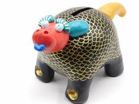 Front view showing black body with gold scale pattern, red head with decorative eyes and blue tongue, yellow tail and gold accented paws, coin slot visible on back.