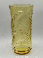 Tall yellow crystal vase with floral cut designs shown straight on with white background.