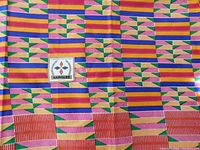 Photo of African Kente patterned fabric showing geometric wax print design in multicolored pattern, including purple, green, red, yellow and white.