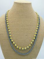 Front view of double strands with silver/gray and mellow yellow faux pearls on display stand.