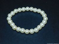 Photo shows a circular stretch bracelet of cream-colored imitation pearls set against a dark background, highlighting the pearl size and luster.