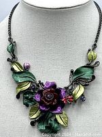 Full view of the necklace on a display bust showing the floral design centerpiece with green and yellow enamel leaves and colored rhinestones.