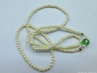 Full view of the 28-inch necklace showing the full length of cream-colored simulated pearls with green crystal bead near the clasp.