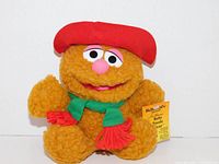 Front view of Baby Fozzie Bear plush showing orange textured plush, red hat, green scarf, and yellow McDonald's promotional tag attached.