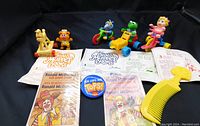 Four Muppet Babies toys with their own toys in packaging, two Ronald McDonald transfer scenes, a McD button, and a yellow comb on black background.