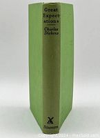 Spine of the green hardcover book with black printed title and author "Great Expectations Charles Dickens" and publisher logo Heinemann.