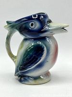 Side angle of the vintage ceramic Kookaburra pitcher showing blue and green glaze details with a handle shaped like the bird's tail and a beak as a spout.