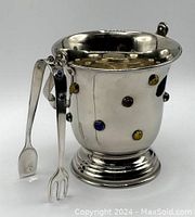 Silver tone studded ice bucket with colorful round stones or beads all around and matching tongs resting on the bucket.