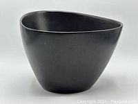 Front and side view showing the smooth matte black finish, irregular three-sided shape, and overall form of the ceramic plant pot.