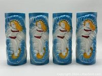 Four ceramic tiki mugs in a row showing surfer girl design on the front in red bikini on blue and white wave background.
