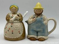 Farmer and wife ceramic sugar bowl and creamer set from front view showing detail and color, cream and brown dress with floral print on wife, blue overalls and yellow hat on farmer.