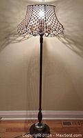 Full view of the vintage floor lamp standing on wooden floor with wall background, showing assembled lamp with macrame shade on top and round base.