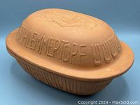 View of clay cookware with lid upside down showing raised 'SCHLEMMERTOPF' lettering on lid rim and flat base surface.