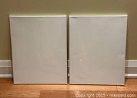 Front views of two white artist canvases side by side on a wood floor against a wall, showing sealed white surfaces.