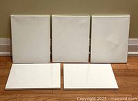 Five artist canvases arranged with three standing upright and two laying flat, showing their white surfaces and wood frames.