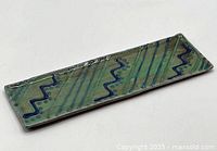 Top diagonal view of rectangular ceramic tray showing blue zigzag and striped pattern on green glaze base.