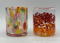 Two colourful hand blown glass candle holders side by side, showing distinct splatter patterns on clear glass.