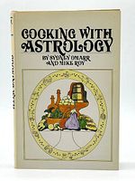 Front cover of the hardcover book 'Cooking With Astrology' showing illustrated food items and title with author names.