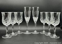 Eight cut glass stemware pieces in two sizes and patterns arranged in a row against black background