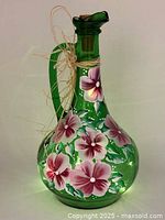 Front view of green glass jug with handpainted purple and pink flowers and a raffia bow tied on the handle.