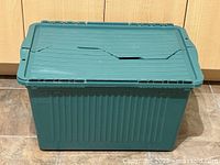 Front view of green plastic storage bin with hinged lid, showing the ribbed sides and the attached lid with hinge details.