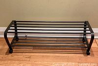 Side view of the dark brown metal two-level shoe rack on wood floor showing the bars and curved end frame.