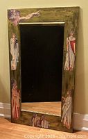 Full view of the large rectangular mirror with burnished gold wood frame and decoupaged art figures on the edges.