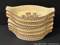 Stack of six oval ceramic baking dishes showing brown trim and cream color with floral design inside
