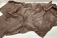 Two irregular pieces of chocolate brown leather laid flat showing texture and shape.