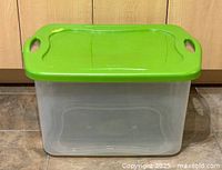 Closed clear storage bin with green lid on top, corner view shows rectangular shape and handles.