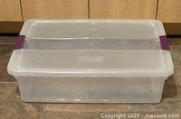 Clear Sterilite plastic storage bin with purple snap-on lid shown closed on kitchen floor.