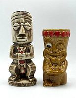 Front view of two tiki mugs, beige Tiki Dumb holding small beaver figure, and brown Tiki Zombie Beaver with red flower crown.