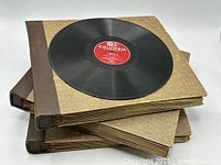 Three large vintage binders stacked, each holding numerous 78 RPM records; the top binder partially open showing a black vinyl record with a red Columbia label.