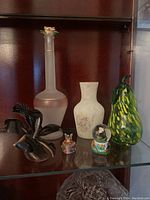 Displaying the glass vases, black glass flower sculpture, and small figurines on the shelf
