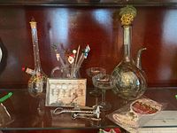 Display of barware including glass wine chiller, cocktail glasses, decorative swizzle sticks, corkscrew, and other accessories on wooden shelf.