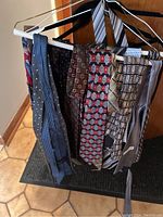 Multiple men's ties and leather belts hanging on hangers showing patterns and colors.