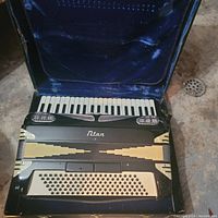 Top-down view of black Titan accordion inside blue velvet-lined case, showing piano keys, bass buttons, and decorative front grille.