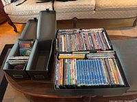 Overview photo showing two black storage boxes on a table with DVDs stored in cases inside and some loose discs visible.
