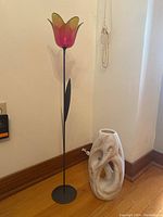 Flower sculpture with pink and green glass petals on black stem and round steel base, alongside a white marbled ceramic vase with abstract design.