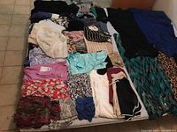 Photo showing a range of ladies clothing including blouses, shorts, and dresses laid out on a bed.