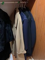 Five vintage coats hanging on a closet rod, mostly wool and medium size, showing a range of colors including black, beige, navy, and dark colors.