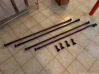 Four wooden curtain rods and four matching wooden rod holders arranged on tiled floor in basement. One rod has a loose finial knob as noted.