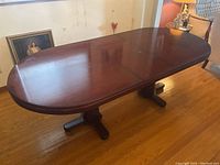 Mahogany oval dining table extended to 86 inches with leaf inserted, showing polished top and double pedestal base.