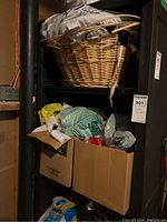 Wicker basket filled with fabric pieces placed on a shelf above two cardboard boxes also filled with fabric pieces and bags.