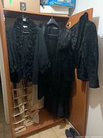 Three black outerwear items hanging in a wardrobe: two faux fur coats and one knit jacket with ruffled fur trim.