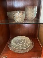 Clear glass bowls with diamond-cut pattern stacked on left and right, clear decorative glass plates stacked below.