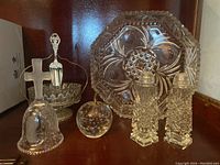 Wide view showing all items in the lot: cut glass bowl, salt and pepper shakers, glass bell with cross, small bowl with spoon, and apple-shaped paperweight.