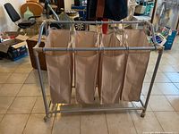Photo of the laundry sorter showing the front view with four beige fabric bags suspended from the metal frame.