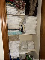 Photo shows three shelves with folded white towels in different sizes, beige flannel sheets, patterned and plain pillowcases, and decorative pillows in brown and red tones.